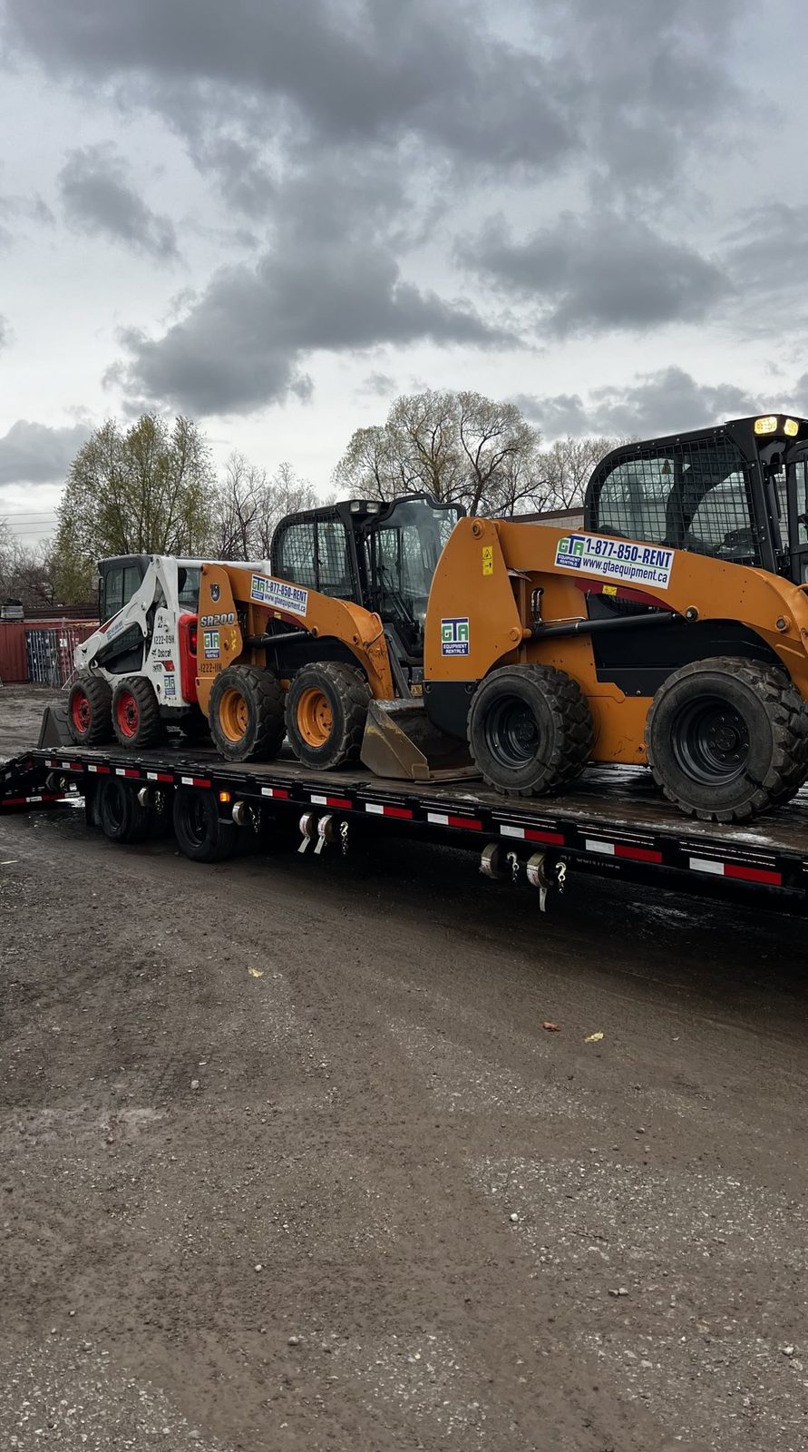 Two skid steers loaded on the GTA Equipment Rentals float trailer